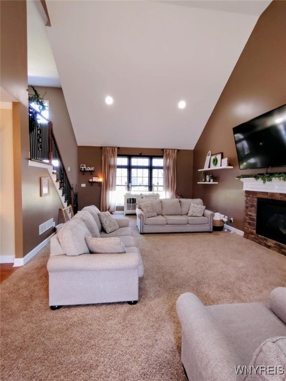 carpeted living area featuring visible vents, baseboards, a stone fireplace, high vaulted ceiling, and stairway