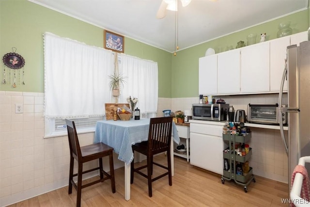 kitchen with a toaster, tile walls, white cabinets, light wood finished floors, and appliances with stainless steel finishes