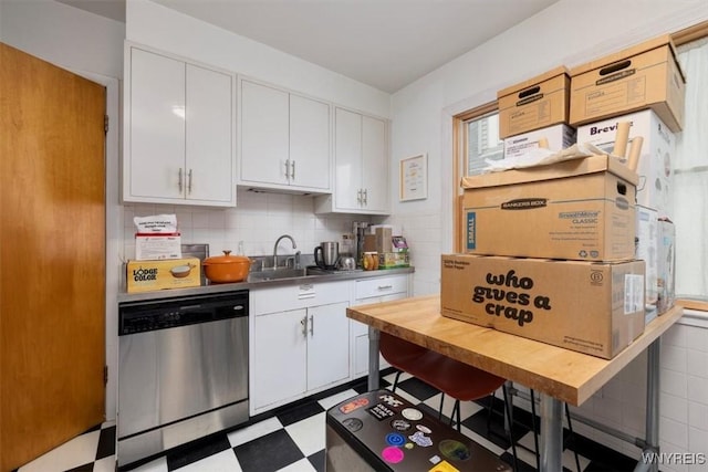 kitchen with stainless steel dishwasher, tile patterned floors, a sink, and white cabinets