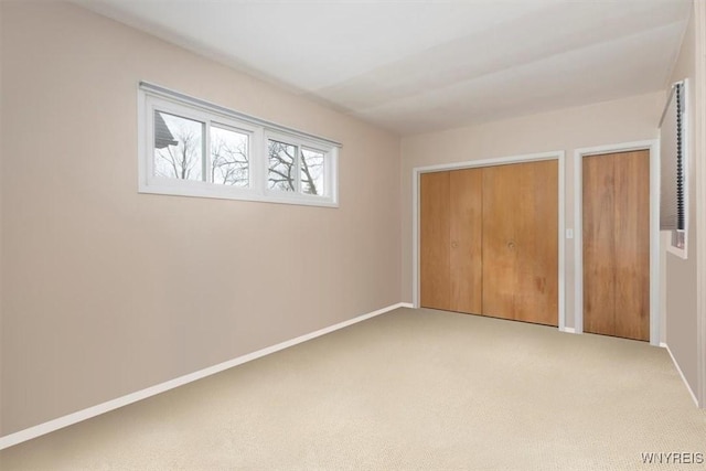 unfurnished bedroom with light colored carpet, baseboards, and two closets