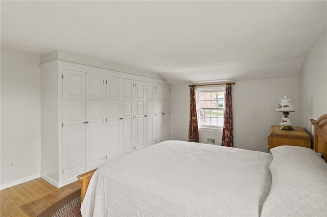 bedroom featuring light wood-style floors, baseboards, and lofted ceiling