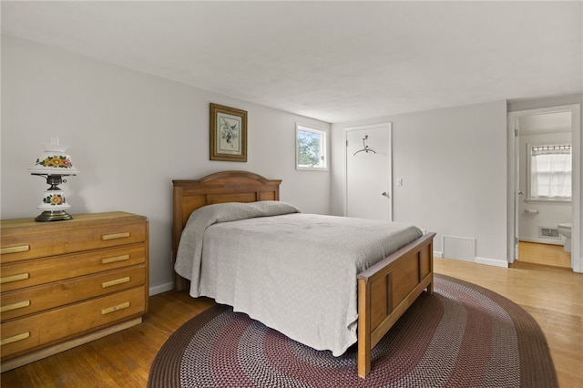 bedroom with visible vents, baseboards, connected bathroom, and wood finished floors