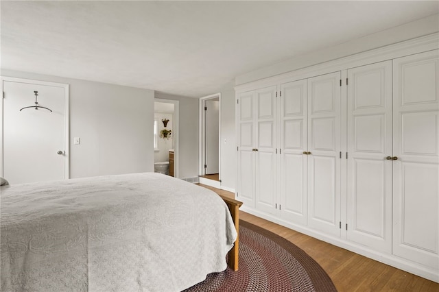 bedroom with ensuite bathroom, multiple closets, and wood finished floors