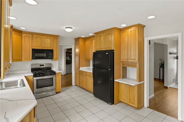 kitchen featuring light stone countertops, a sink, recessed lighting, light tile patterned floors, and black appliances