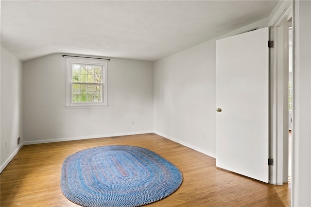 empty room featuring baseboards, vaulted ceiling, and wood finished floors