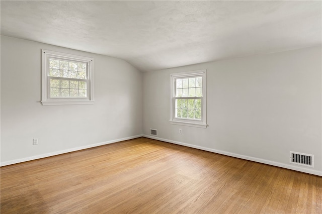 empty room featuring visible vents, baseboards, lofted ceiling, and wood finished floors