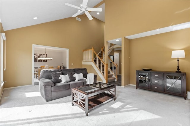 living area with high vaulted ceiling, ceiling fan with notable chandelier, stairs, and light colored carpet