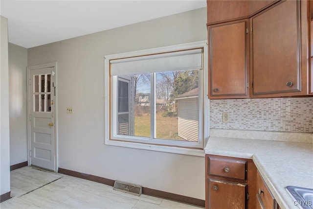 kitchen featuring visible vents, brown cabinetry, baseboards, light countertops, and backsplash
