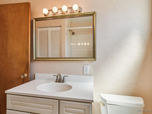 bathroom featuring vanity, a textured wall, walk in shower, and toilet