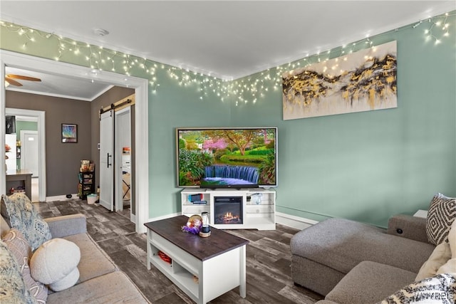 living area featuring baseboards, a barn door, a glass covered fireplace, and crown molding