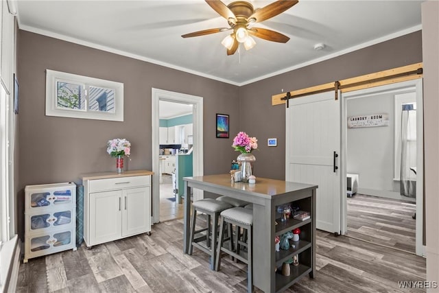 dining room with ceiling fan, a barn door, wood finished floors, and ornamental molding