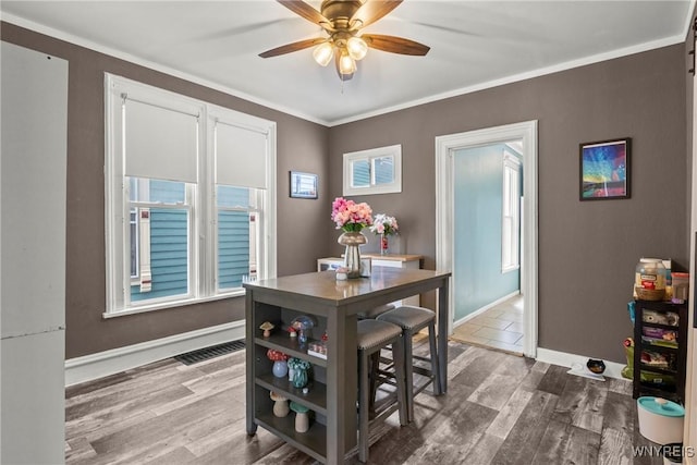 dining area featuring crown molding, baseboards, a ceiling fan, and wood finished floors