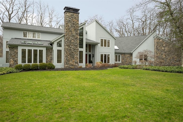 rear view of property with a yard, roof with shingles, a chimney, and stone siding