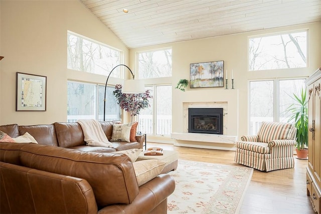 living area featuring a glass covered fireplace, high vaulted ceiling, light wood finished floors, and wooden ceiling