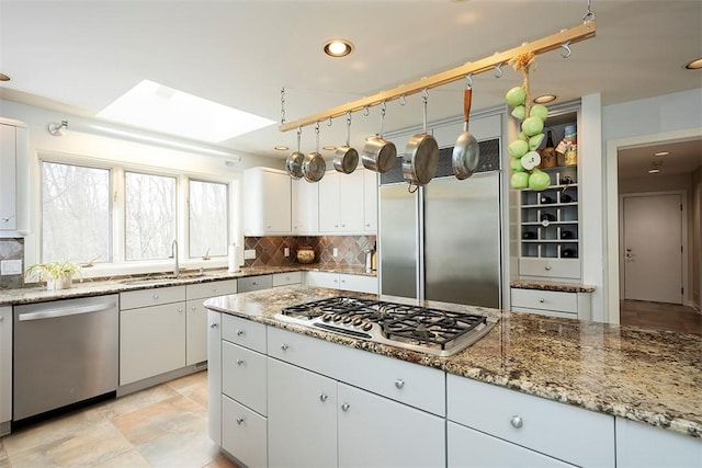 kitchen with a sink, backsplash, stainless steel appliances, and white cabinetry