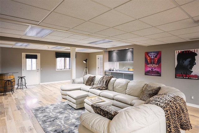 living room featuring light wood-style floors, baseboards, and a drop ceiling
