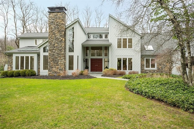 view of front of property featuring a shingled roof, a front lawn, stone siding, and a chimney