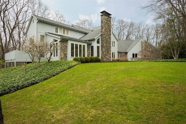 back of house featuring a chimney, a yard, and stone siding