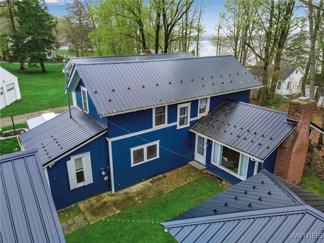 back of property featuring a yard, a chimney, and metal roof