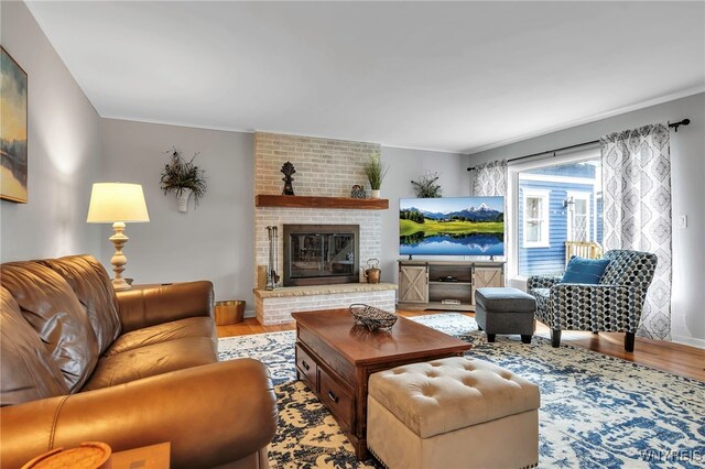 living area featuring crown molding, a brick fireplace, and light wood-style flooring