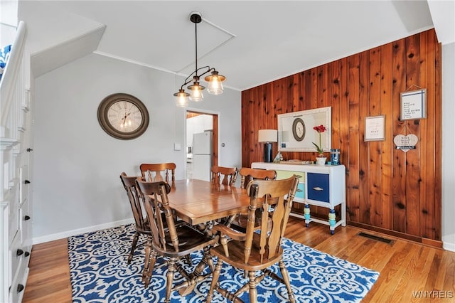 dining space featuring visible vents, baseboards, wood finished floors, and wooden walls