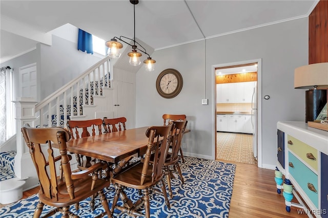 dining space featuring baseboards, ornamental molding, light wood-type flooring, and stairs