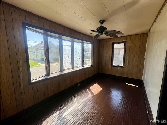 spare room with baseboards, wood walls, dark wood finished floors, and a ceiling fan