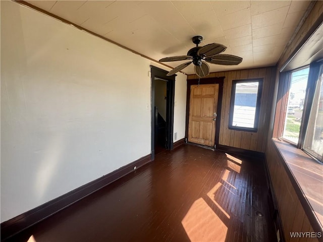 empty room featuring a ceiling fan, baseboards, and dark wood-style floors