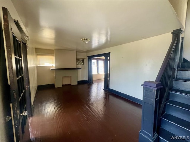 unfurnished living room with stairs, baseboards, and dark wood finished floors