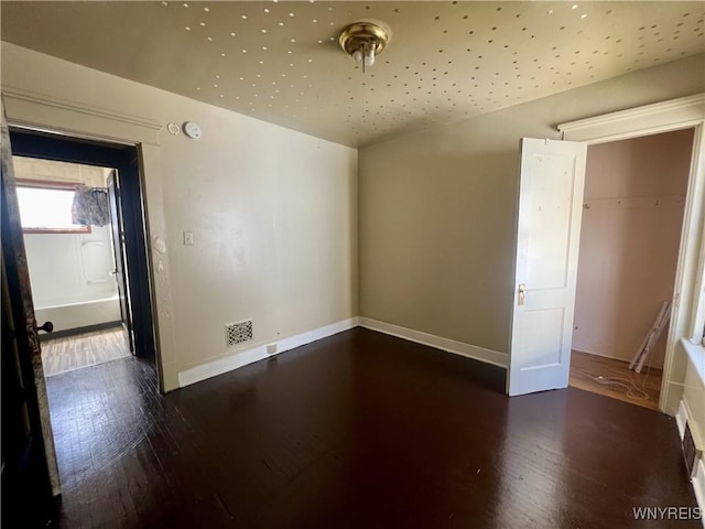 empty room with baseboards, vaulted ceiling, wood finished floors, and visible vents