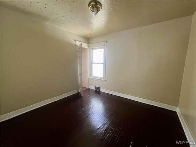 spare room with baseboards, wood finished floors, and visible vents