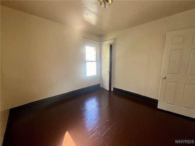 empty room featuring baseboards and dark wood-type flooring