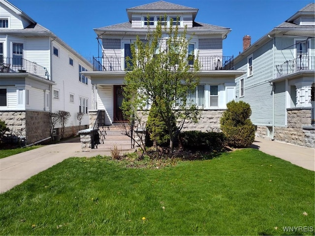 american foursquare style home featuring a shingled roof, a balcony, and a front yard