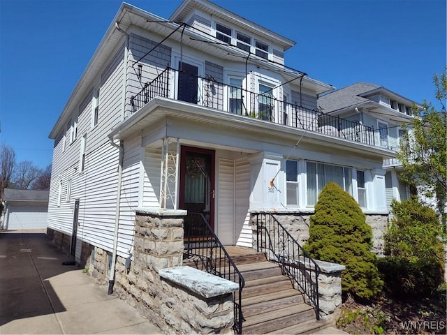 view of front of house with a detached garage, an outbuilding, and a balcony