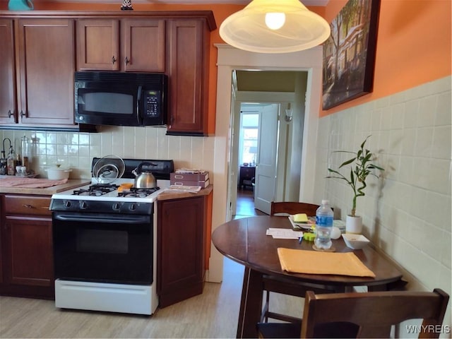 kitchen featuring decorative backsplash, gas range, black microwave, light wood-type flooring, and light countertops