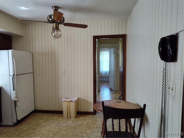 kitchen featuring freestanding refrigerator, wooden walls, and ceiling fan