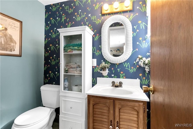 bathroom featuring vanity, toilet, and wallpapered walls