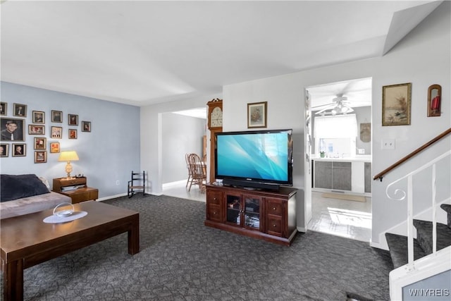 carpeted living room with baseboards, a ceiling fan, and stairs