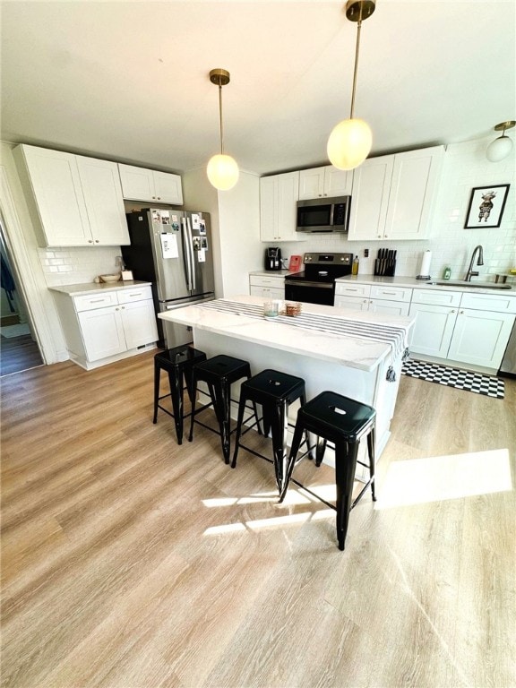 kitchen featuring tasteful backsplash, light wood-type flooring, a sink, stainless steel appliances, and white cabinetry