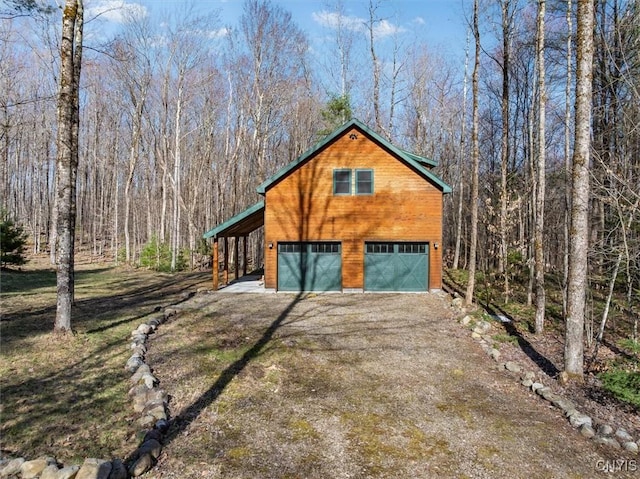 exterior space featuring a detached garage, dirt driveway, and a forest view