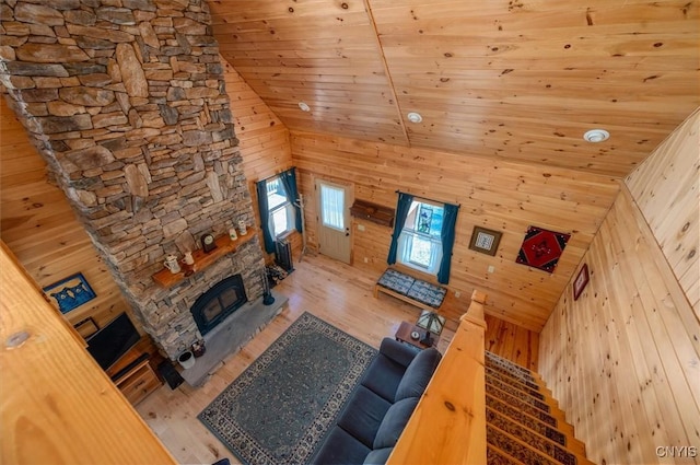 living room with wooden walls, high vaulted ceiling, a stone fireplace, wood finished floors, and wood ceiling