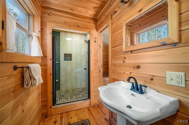 bathroom with a shower stall, a sink, wooden ceiling, wood-type flooring, and wooden walls