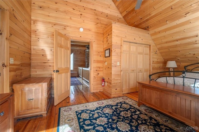 bedroom with vaulted ceiling, wood walls, wooden ceiling, a closet, and light wood-style flooring