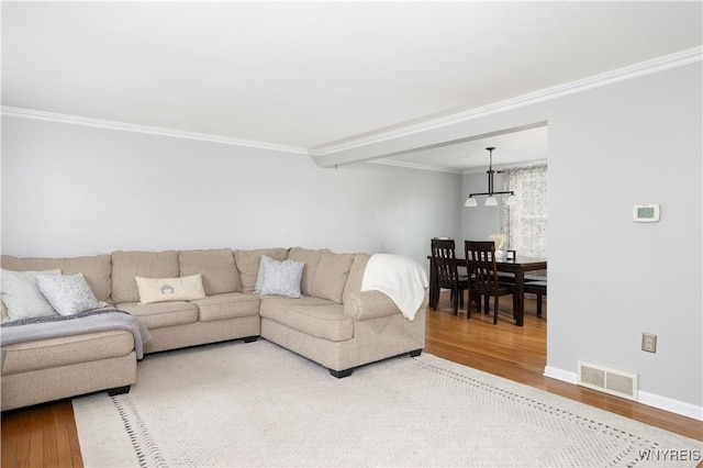 living area featuring visible vents, baseboards, crown molding, and wood finished floors