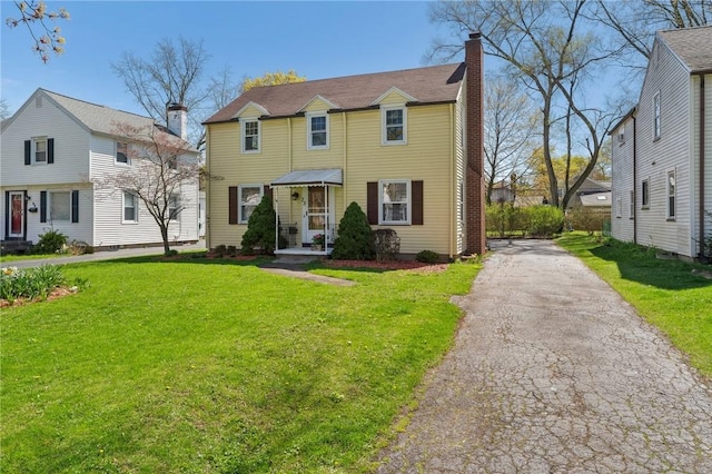 view of front of property featuring a chimney, driveway, and a front lawn