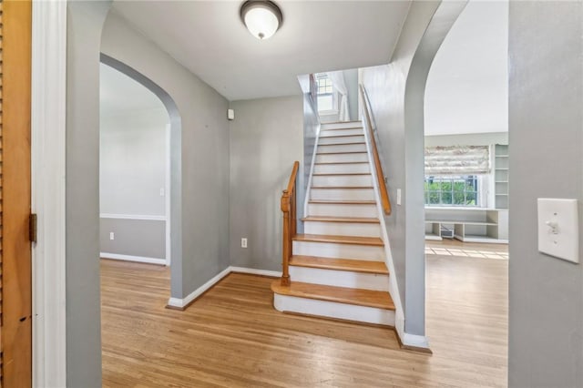 stairs with arched walkways, baseboards, and wood finished floors