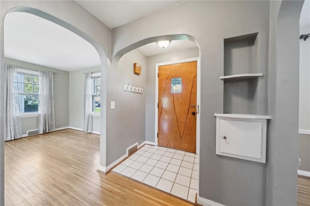 entryway with light wood-style floors, baseboards, arched walkways, and visible vents