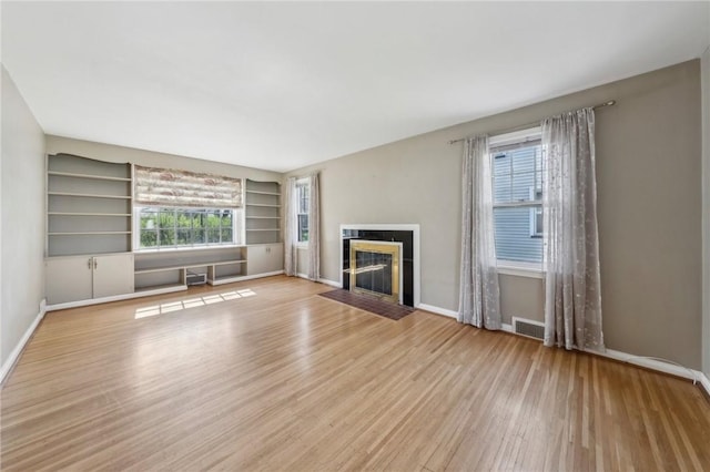 unfurnished living room featuring visible vents, a fireplace with flush hearth, built in features, wood finished floors, and baseboards