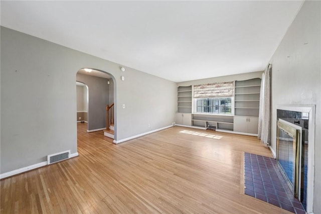 unfurnished living room featuring visible vents, built in features, baseboards, arched walkways, and light wood finished floors