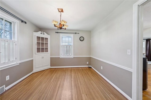 unfurnished dining area with baseboards, visible vents, wood finished floors, and a chandelier